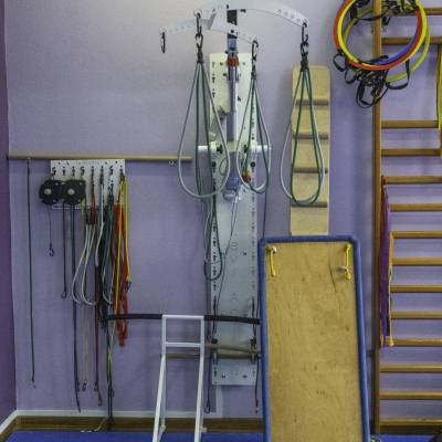 Zbliżenie sprzętu do rehabilitacji: system podwieszeń z pasami, drabinki i drewniana platforma.