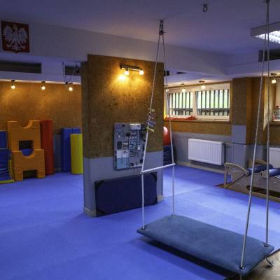 Sala ćwiczeń z niebieskimi matami, huśtawką platformową i piankowymi modułami; ciepłe oświetlenie.